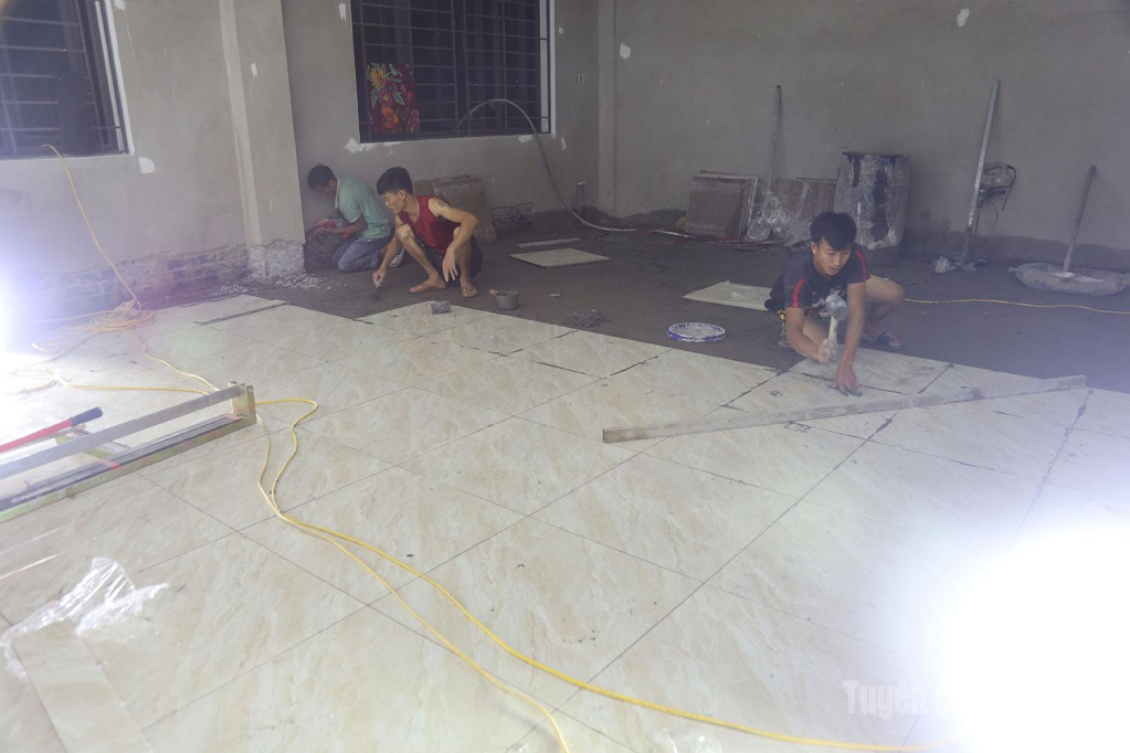 Dưới ánh đèn tổ công nhân khẩn trương lát gạch nền các phòng học.