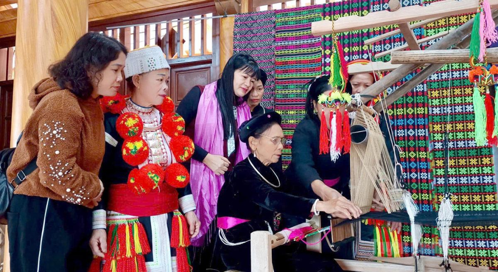 Văn hóa truyền thống bản địa là lợi thế để các làng văn hóa thu hút khách du lịch (Trong ảnh: Khách du lịch thích thú với nghề dệt thổ cẩm truyền thống của đồng bào Tày ở Lâm Bình)