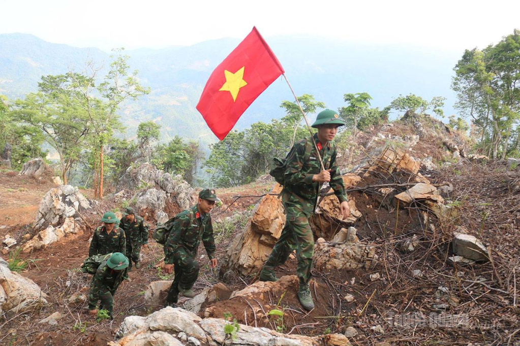 Thiếu tá Vũ Văn Đông (người đi đầu cầm cờ) cùng các đồng đội vượt núi, băng rừng thực hiện nhiệm vụ tìm kiếm, quy tập hài cốt liệt sĩ.